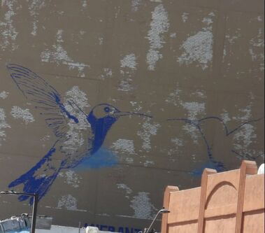 A grey wall with two blue hummingbirds, one detailed and the other just an outline, facing each other.